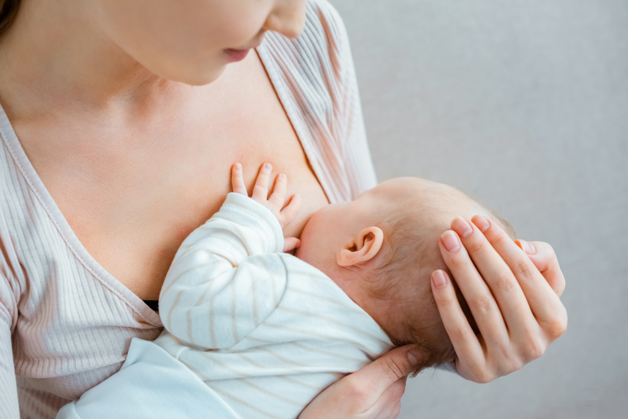 cropped shot of young woman breastfeeding baby on grey