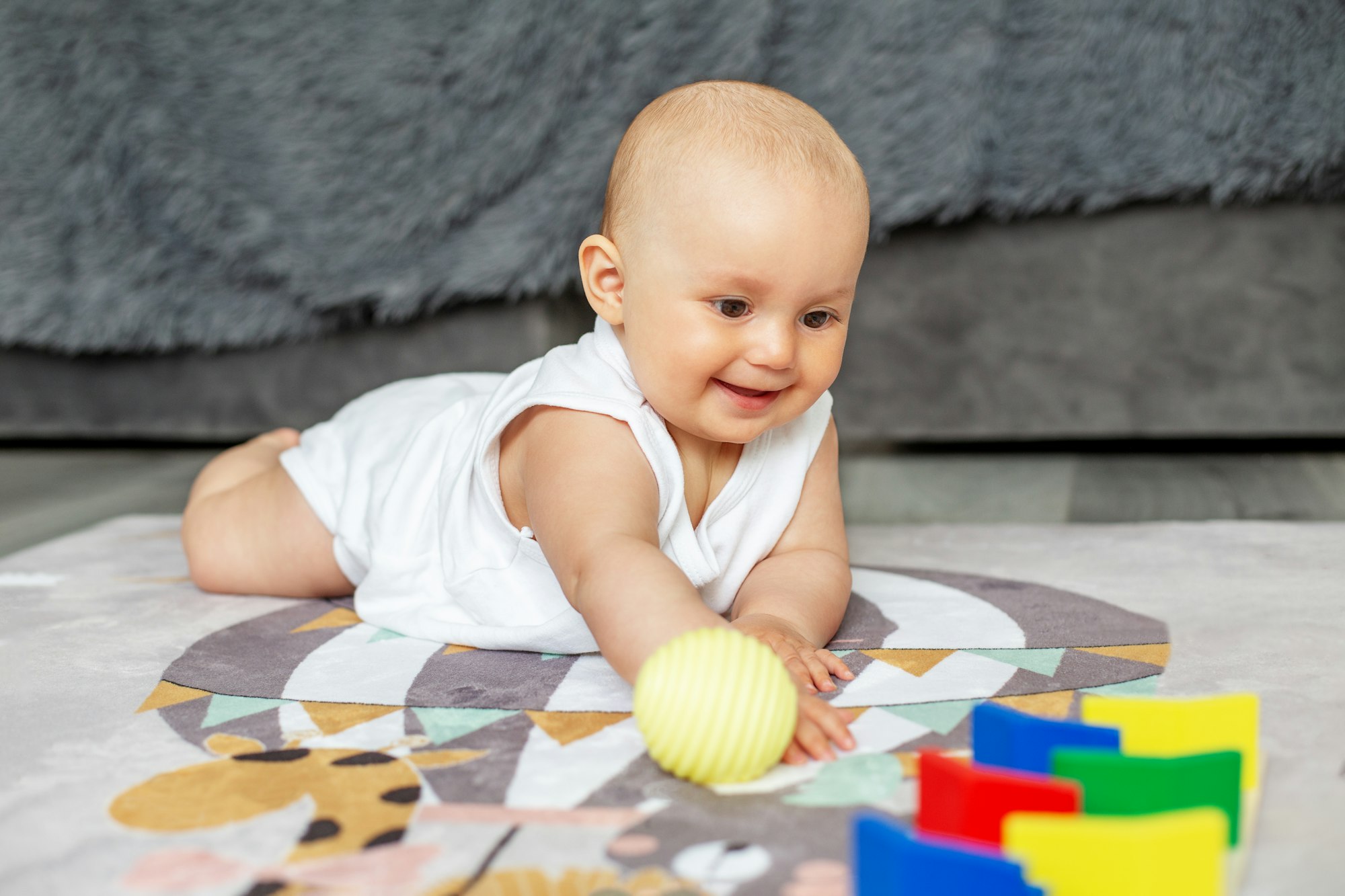 Smiling baby creep on floor of nursery grabbing colorful ball. Baby development. Sensory experience